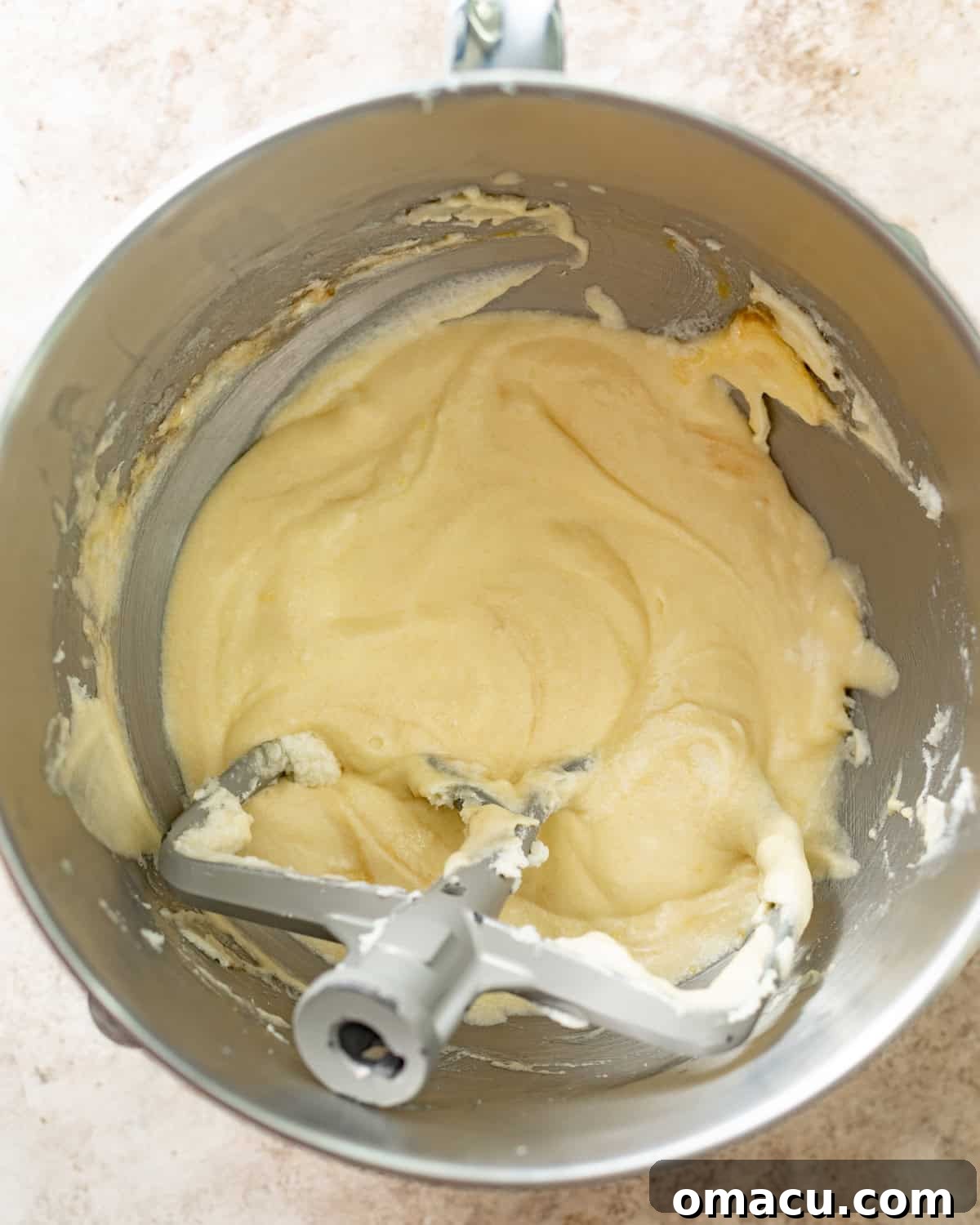A captivating shot of room temperature butter, soft cream cheese, fragrant coconut oil, and fine granulated sugar being expertly creamed together in the bowl of a powerful stand mixer, utilizing the paddle attachment, resulting in a beautifully light and fluffy mixture, indicative of proper aeration.
