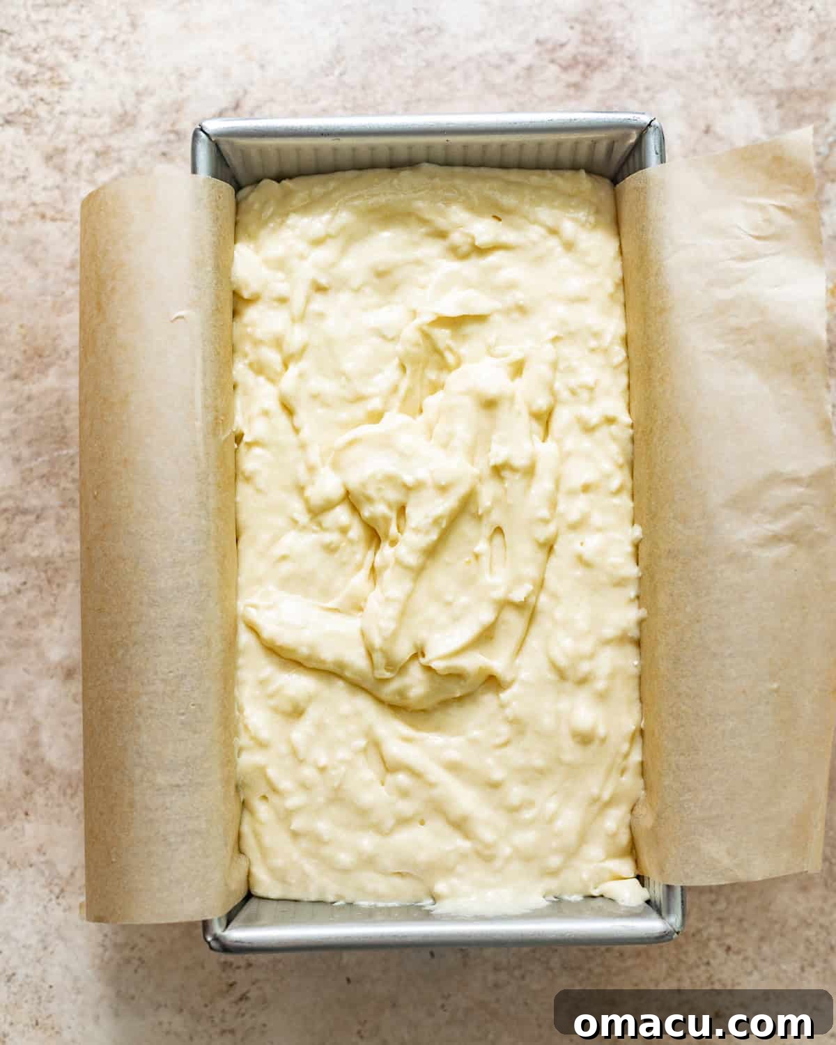 A generous quantity of thick, creamy coconut cake batter being carefully and evenly poured into a parchment-lined loaf pan, poised and ready for its transformation in the hot oven.