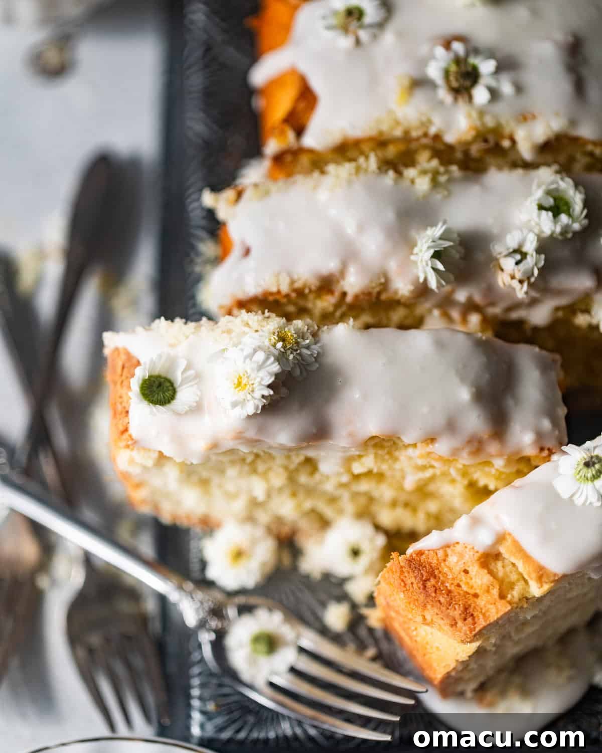 An inviting overhead shot of the beautifully glazed coconut loaf cake, perfectly positioned on a serving plate with a fork nearby, elegantly garnished with vibrant edible flowers, ready to be enjoyed.