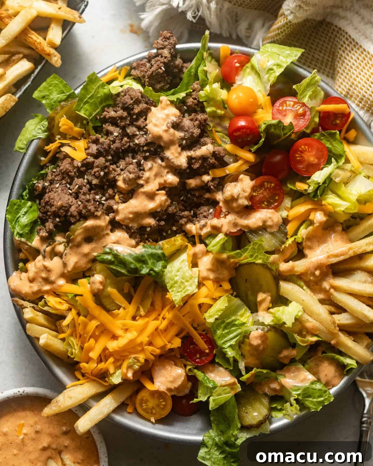 Big Mac Salad in a bowl, served alongside a small portion of french fries and a side of special sauce, ready to be enjoyed.