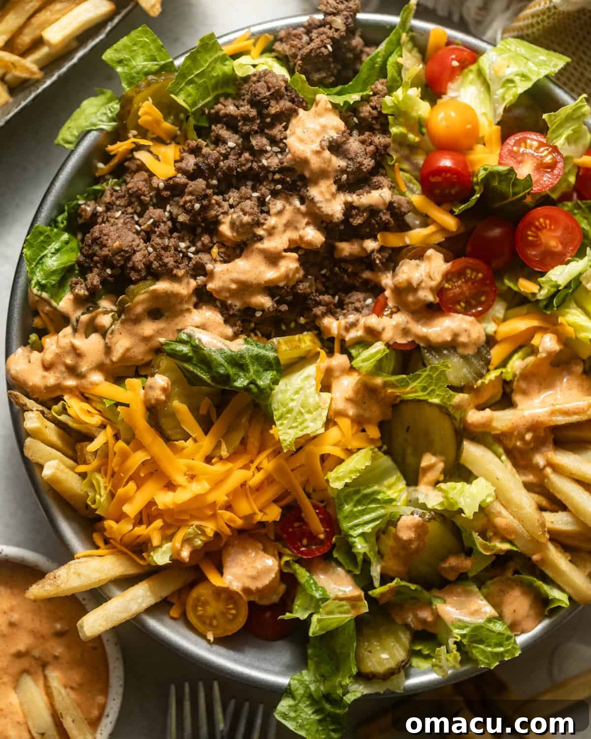 Up-close photo of Big Mac Salad in a serving bowl, showcasing layers of lettuce, ground beef, cheese, tomatoes, pickles, and a generous drizzle of special sauce.