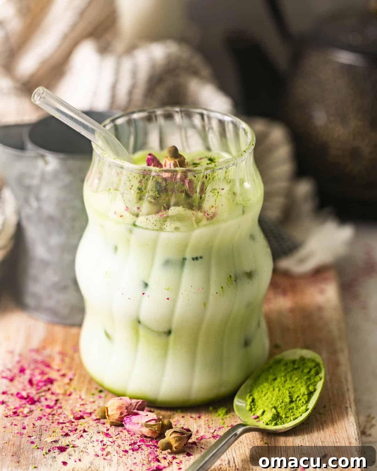 A beautifully prepared Iced Matcha Latte on a rustic cutting board, with a small spoon of bright green matcha powder beside it.