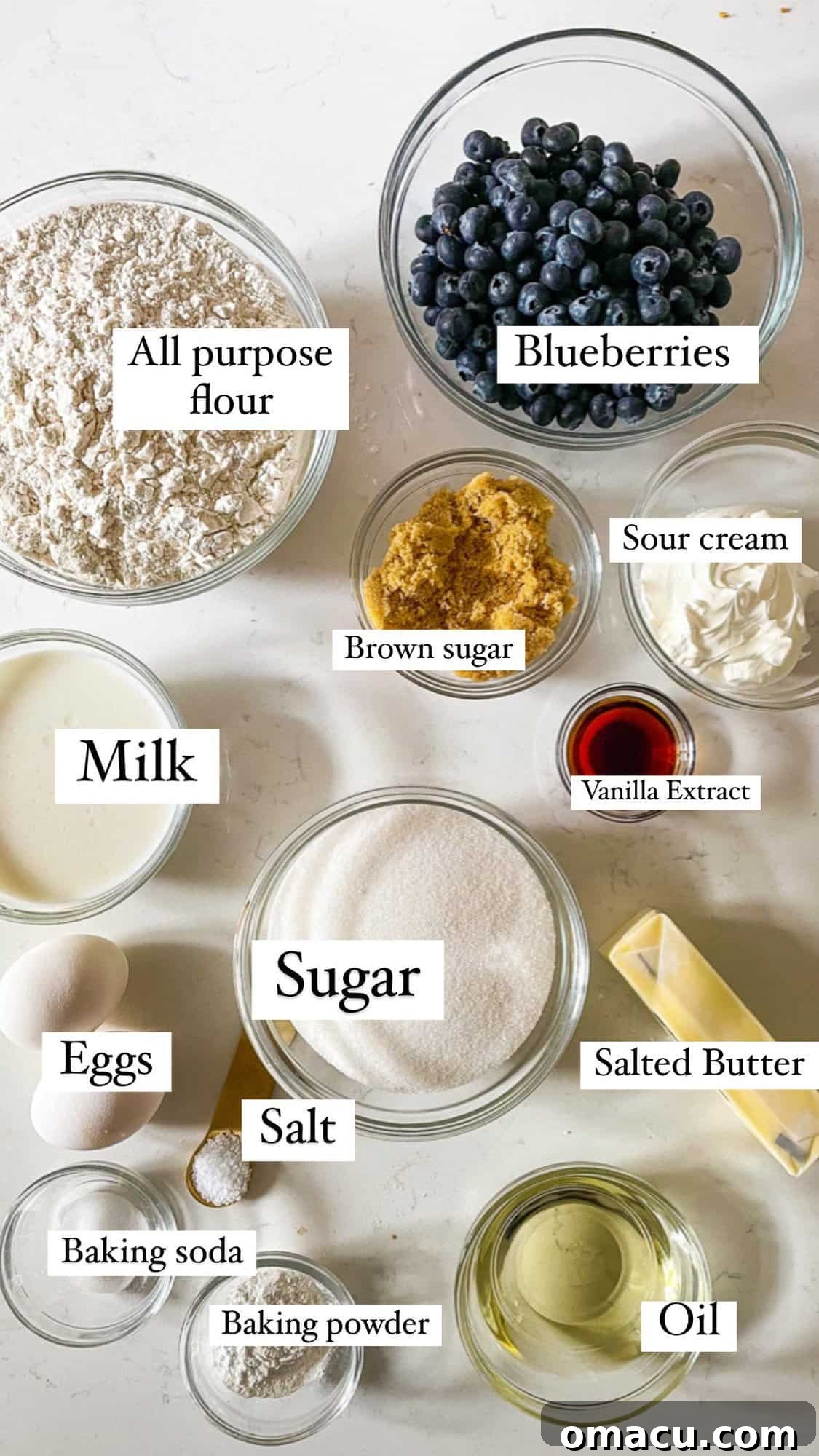 Ingredients for blueberry muffins laid out on a kitchen counter: flour, sugar, butter, sour cream, eggs, blueberries, and leavening agents.