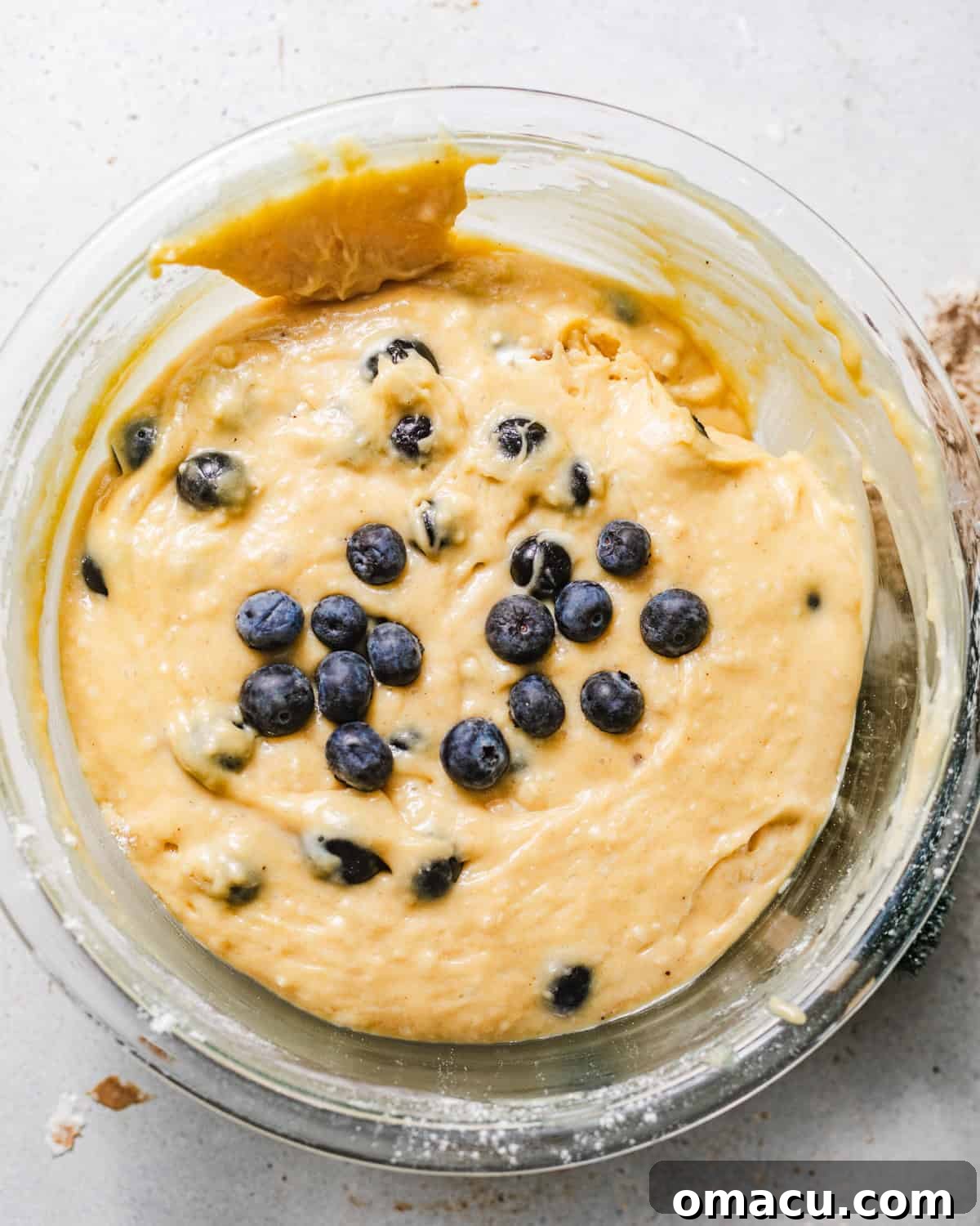 Blueberry muffin batter in a bowl, showing a slightly lumpy texture and blueberries mixed in, covered with a towel for resting.