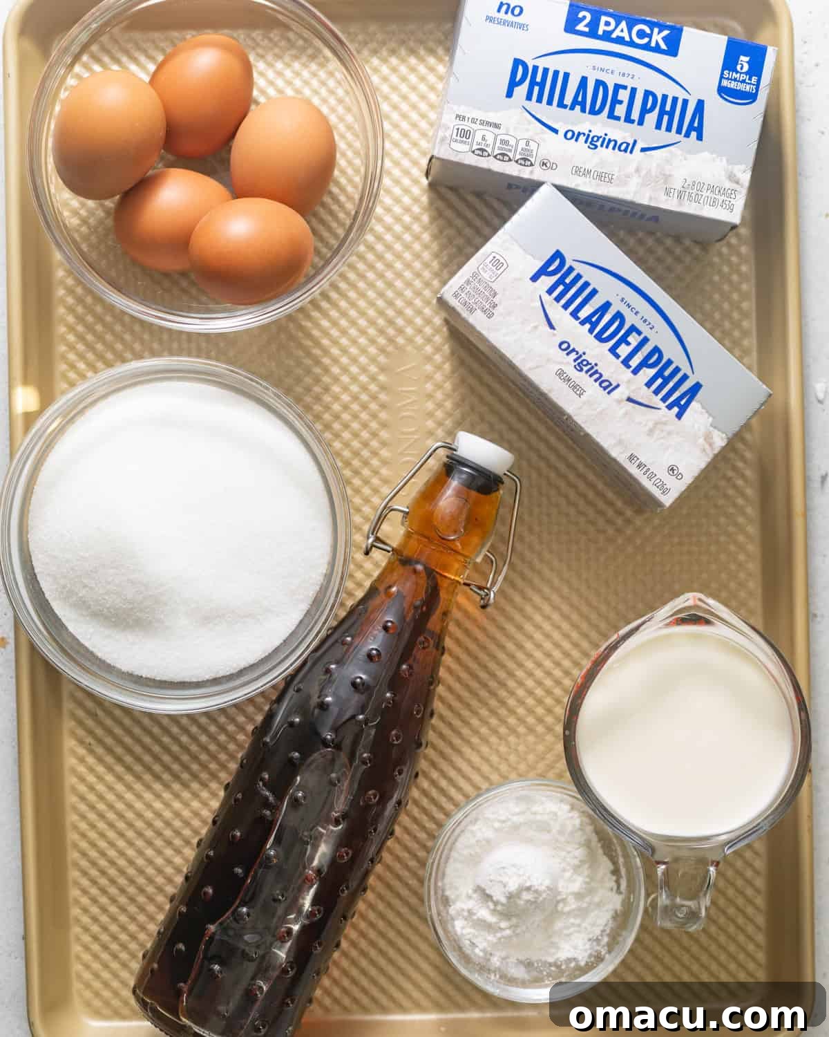 Essential ingredients laid out for making Basque cheesecake: cream cheese, sugar, sour cream, lemon juice, corn starch, flour, vanilla extract, eggs, and heavy cream.