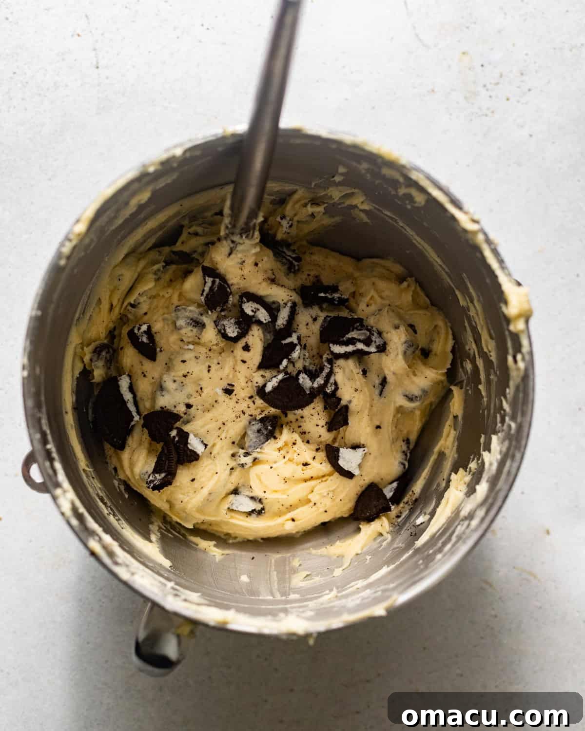 Crushed Oreo cookies being gently folded into the main cake batter in a stand mixer bowl.