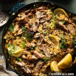 Overhead photo of lemon chicken orzo pasta in a skillet topped with lemons and parsley.