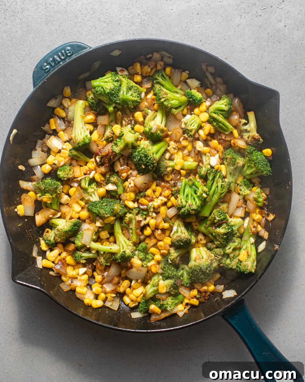 Sautéing broccoli, corn, diced onions, garlic, and seasonings in a skillet.