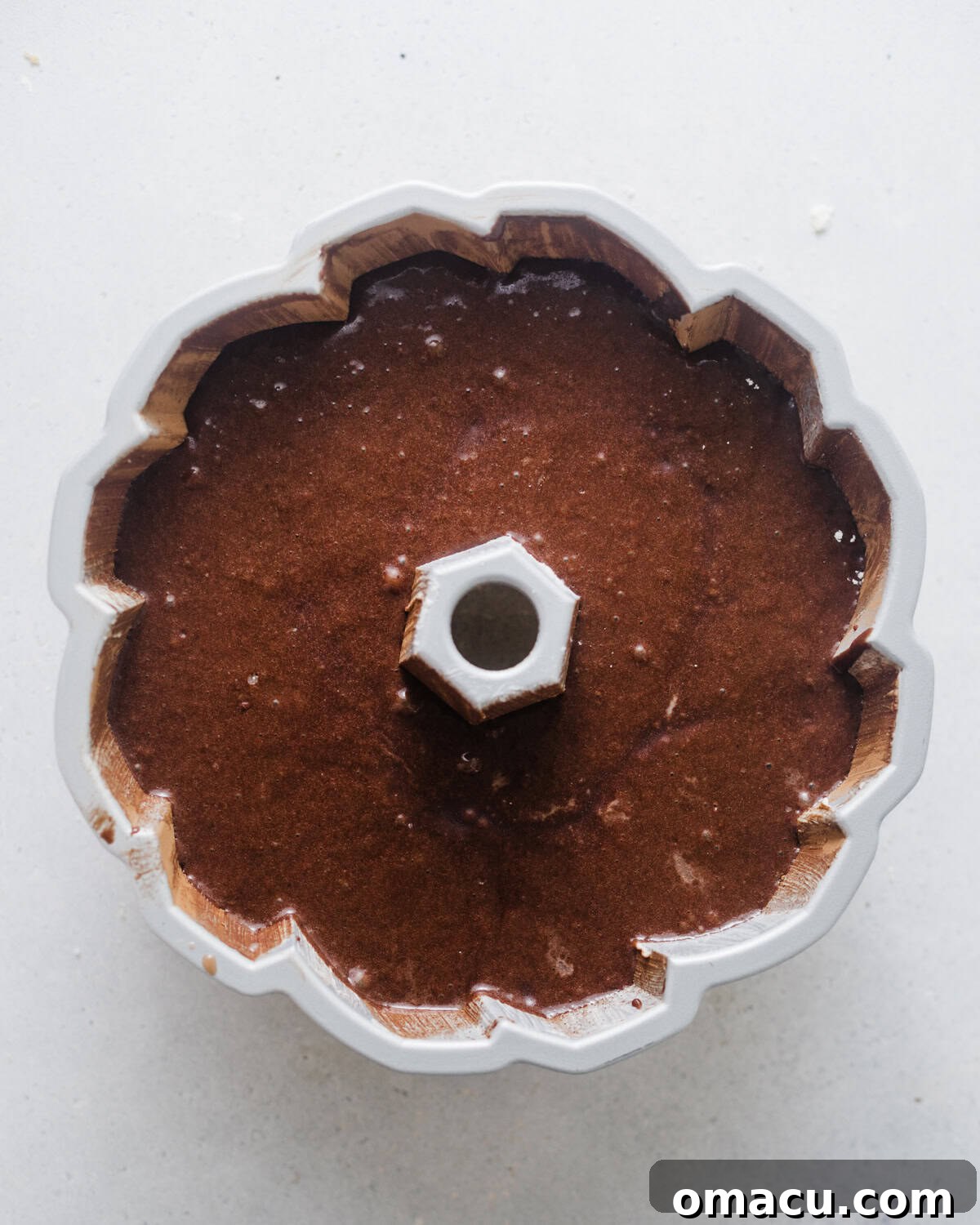 Smooth chocolate cake batter is carefully poured into a meticulously prepared bundt pan, ready to be baked into a delicious donut cake.