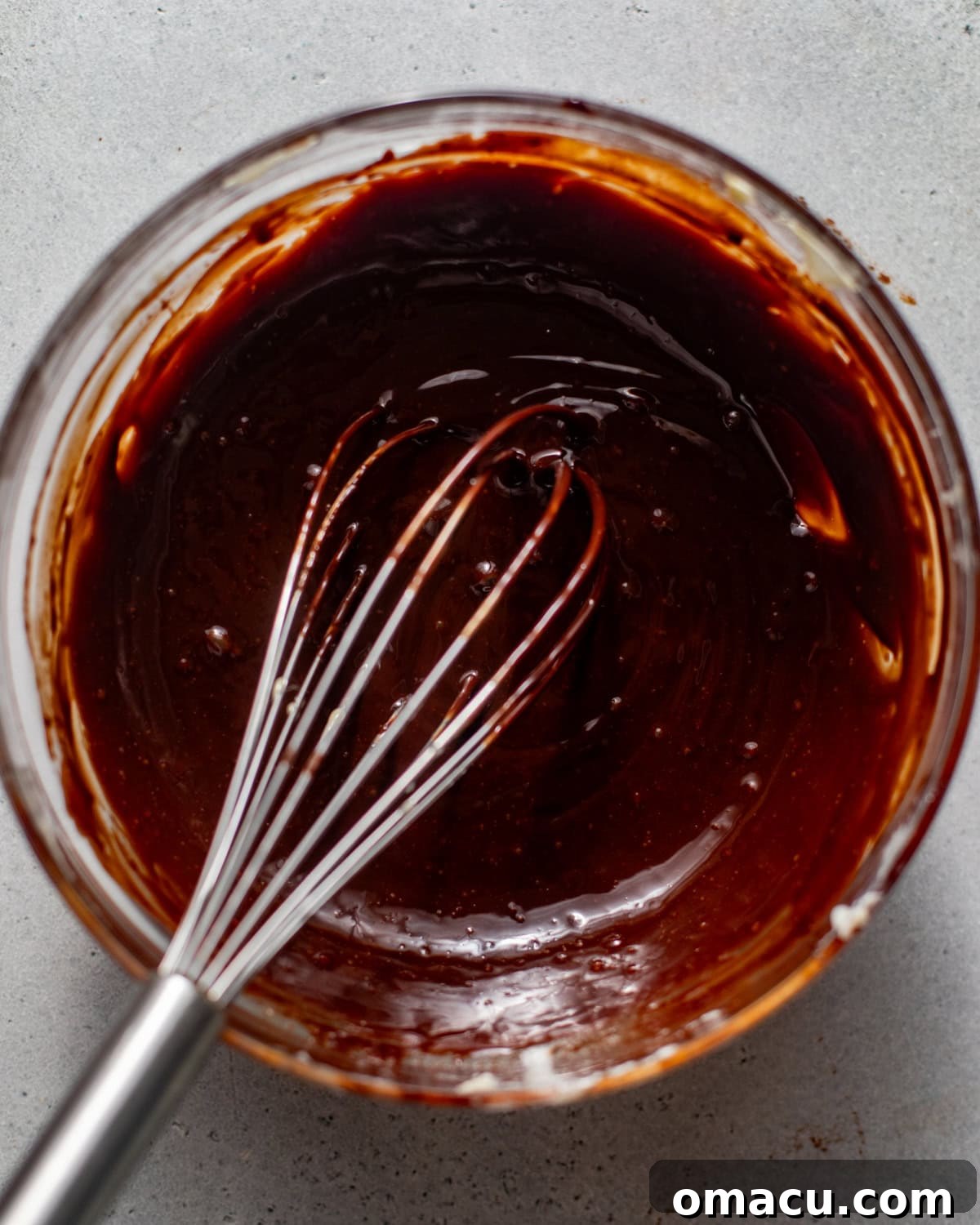 A rich, glossy chocolate glaze is whisked to smooth perfection in a bowl, ready to top the delicious donut cake.
