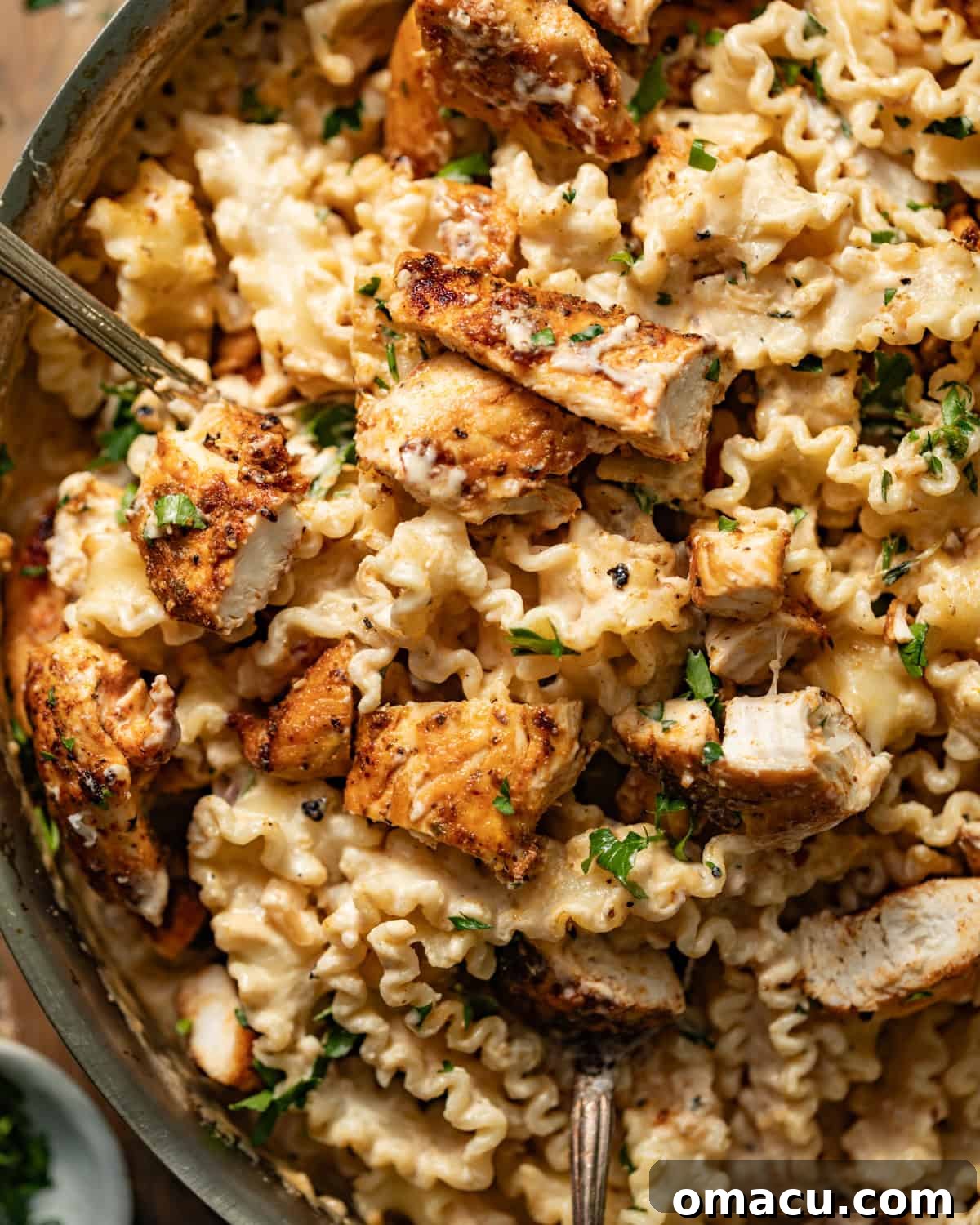 Up close photo of a generous serving of garlic parmesan pasta with chicken on a plate with a spoon, showing the creamy sauce and tender chicken pieces.