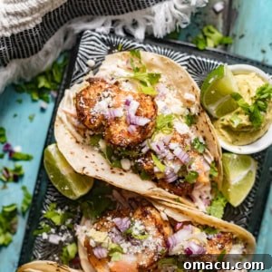 baja shrimp tacos on a serving plate with lime wedges, avocado crema, and a sprinkle of cotija cheese on top.