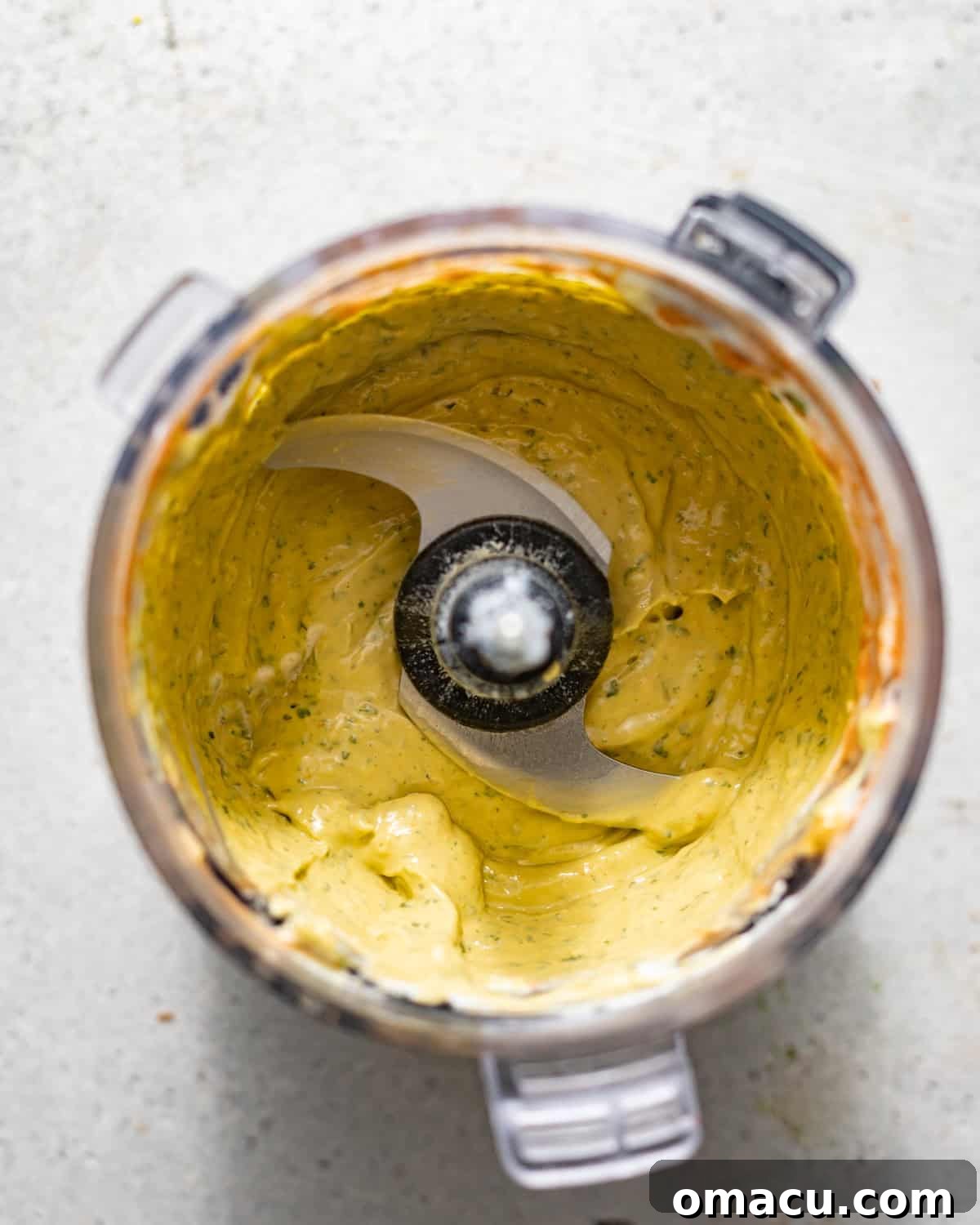 Ripe avocado, sour cream, garlic, cilantro, lime juice, and hot sauce blending into a smooth, creamy avocado crema in a food processor.