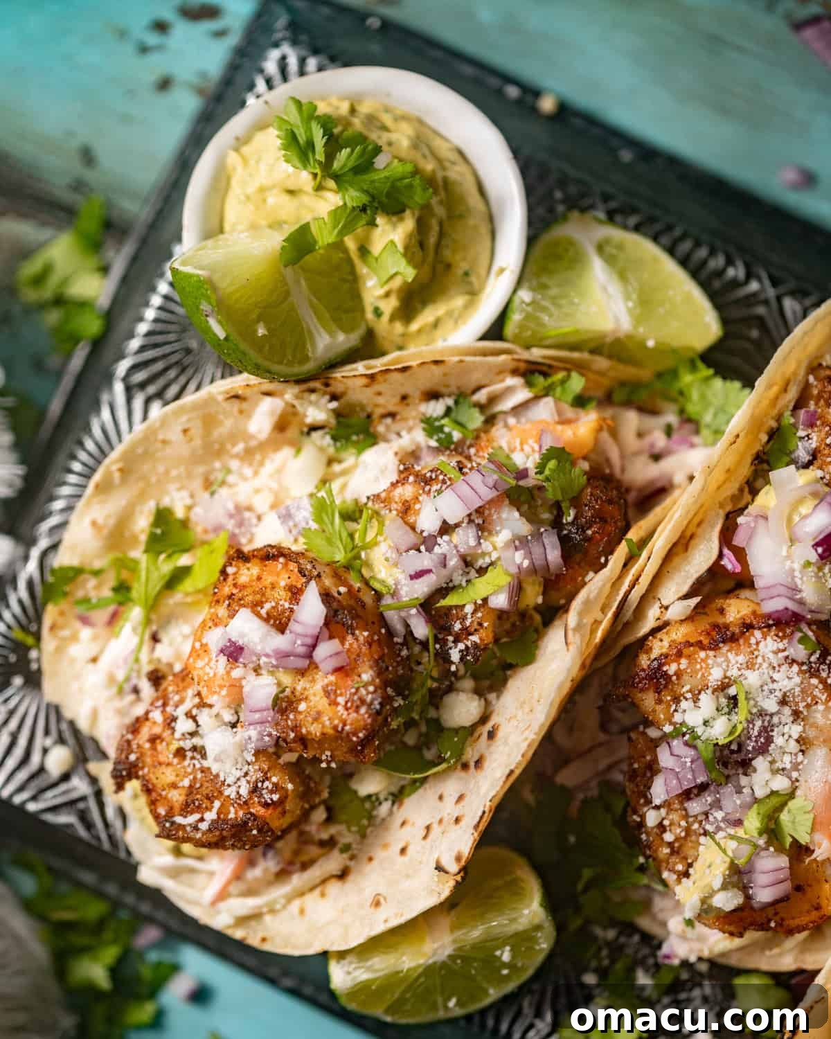 Up close photo of shrimp tacos on a serving dish, highlighting the colorful layers of ingredients and creamy sauce.