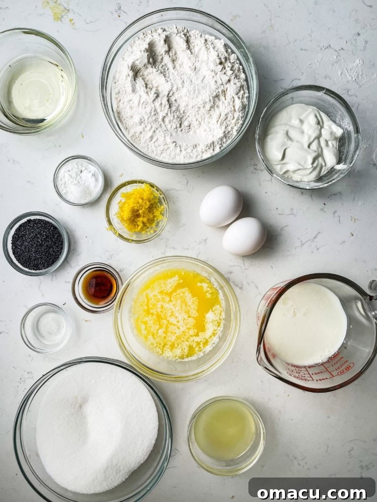 A flat lay of ingredients to make lemon poppy seed cake - cake flour, baking powder, salt, lemon zest, sugar, salted butter, eggs, vanilla extract, olive oil, lemon extract, almond extract, sour cream, cream cheese, powdered sugar, and poppy seeds.