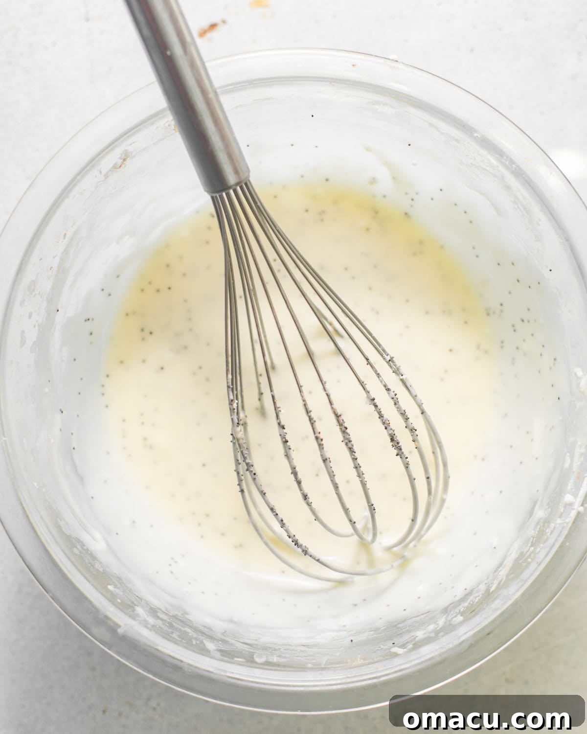 A bowl filled with luscious lemon cream cheese glaze, perfectly smooth and ready to be poured, with a whisk resting in it.