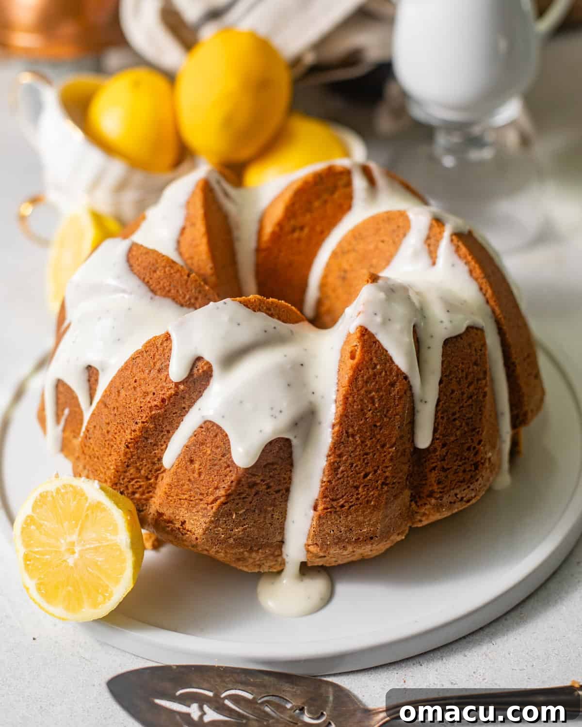 A beautifully glazed lemon poppy seed bundt cake presented on a decorative plate, surrounded by fresh lemon slices and a cake server, ready to be enjoyed.