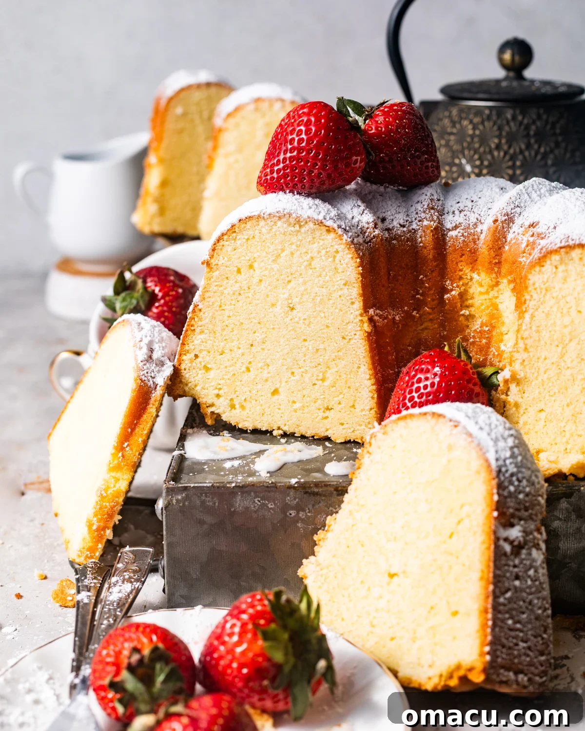 A whole mascarpone pound cake on a wooden table, with several slices coated in powdered sugar arranged beside it.