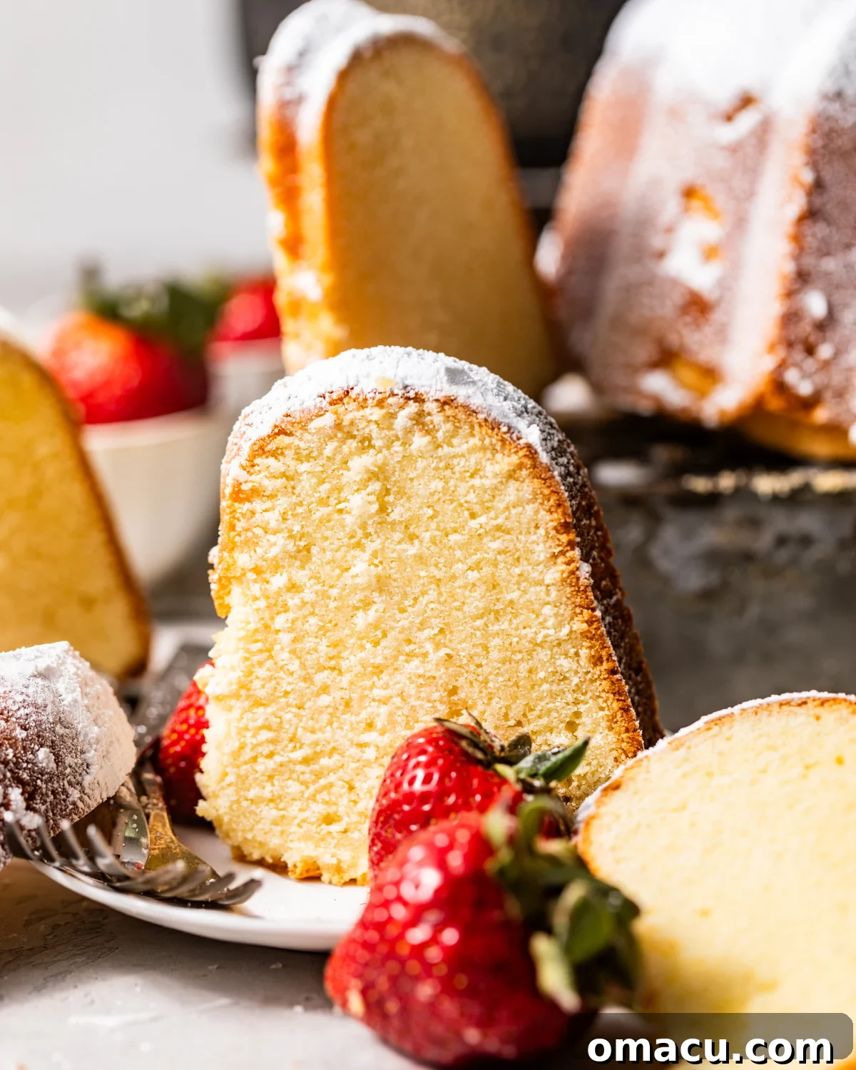 A beautiful slice of mascarpone pound cake served on a white plate with fresh strawberries on the side.