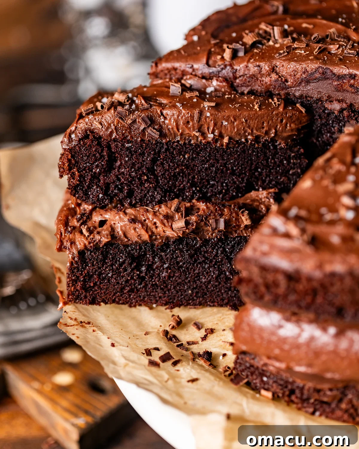 A perfectly sliced chocolate cake with chocolate mousse on top, presented on a pristine cake stand lined with parchment paper.