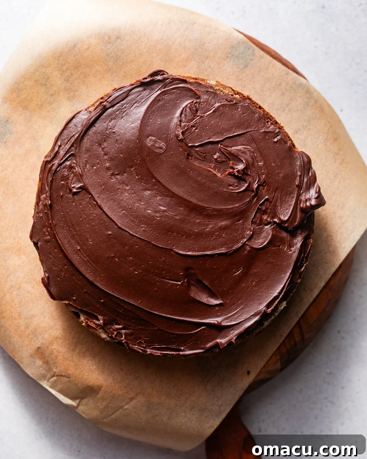 A moist chocolate cake layer topped with a thin, even layer of shiny chocolate ganache, secured in a springform pan.
