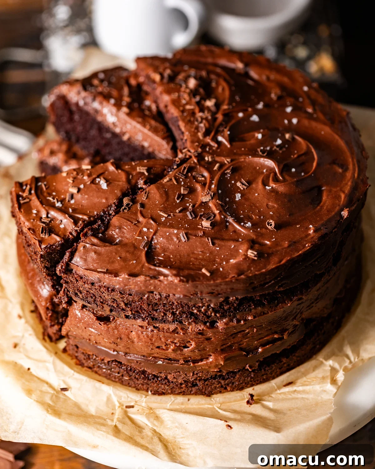 An exquisite chocolate cake with chocolate mousse, beautifully garnished with delicate chocolate curls and a sprinkle of flaky salt, resting on a elegant cake stand.