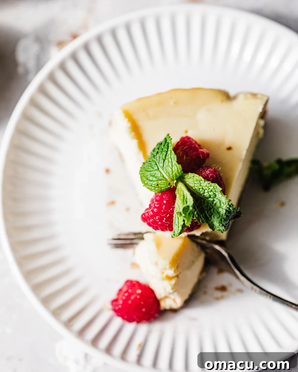 Overhead shot of a mascarpone cheesecake on a white plate, with a fork cutting into a slice, revealing its creamy texture.
