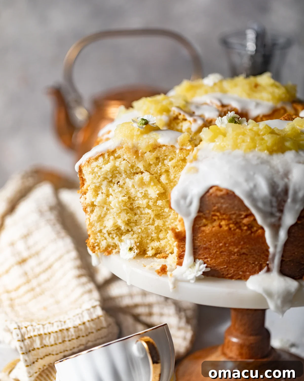 Sliced pineapple pound cake on a cake stand, generously covered in a shimmering pineapple glaze and topped with crushed pineapples for garnish.