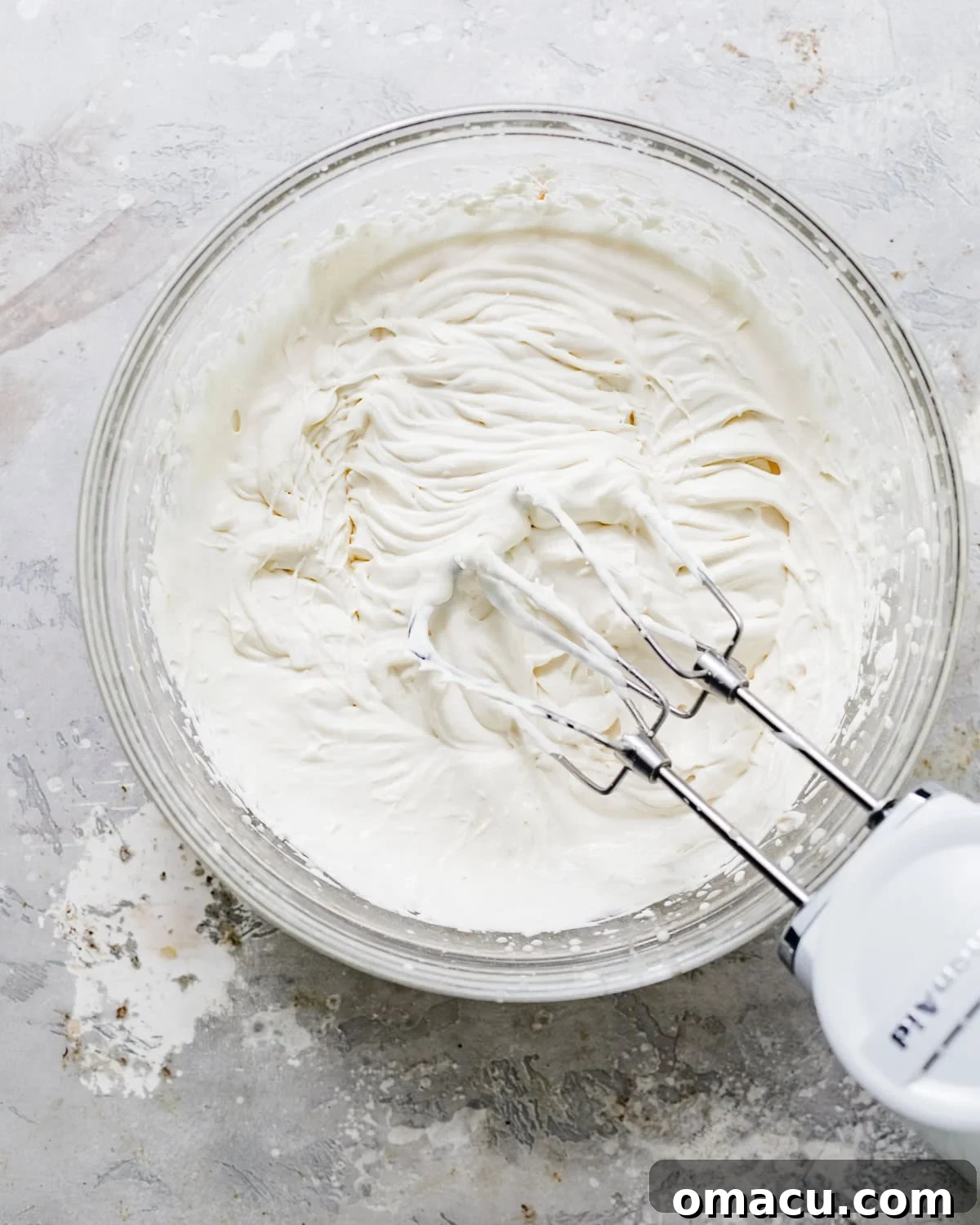 Cold heavy cream and sour cream are being whipped together in a bowl with an electric hand mixer, forming soft peaks.
