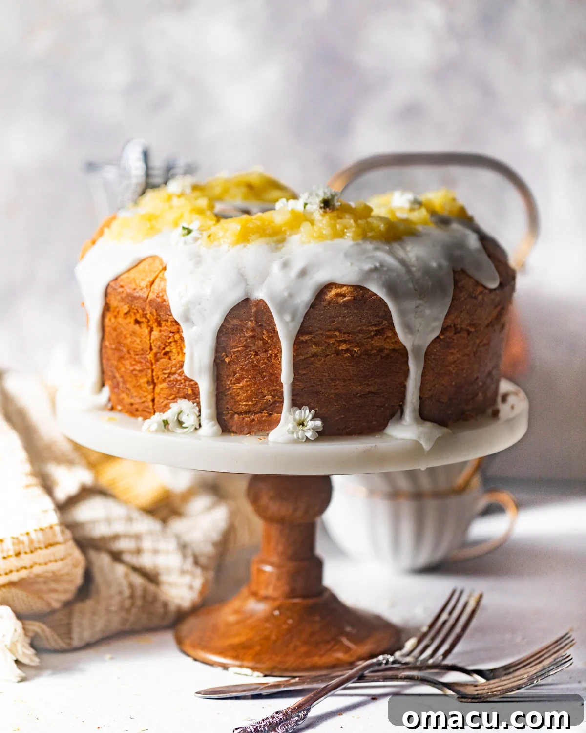 A freshly baked pineapple pound cake, elegantly covered in a smooth, creamy pineapple glaze, presented on a decorative cake stand.
