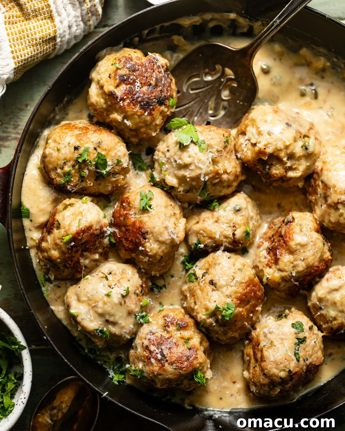 chicken piccata meatballs in a skillet topped with parsley and sliced lemons. 