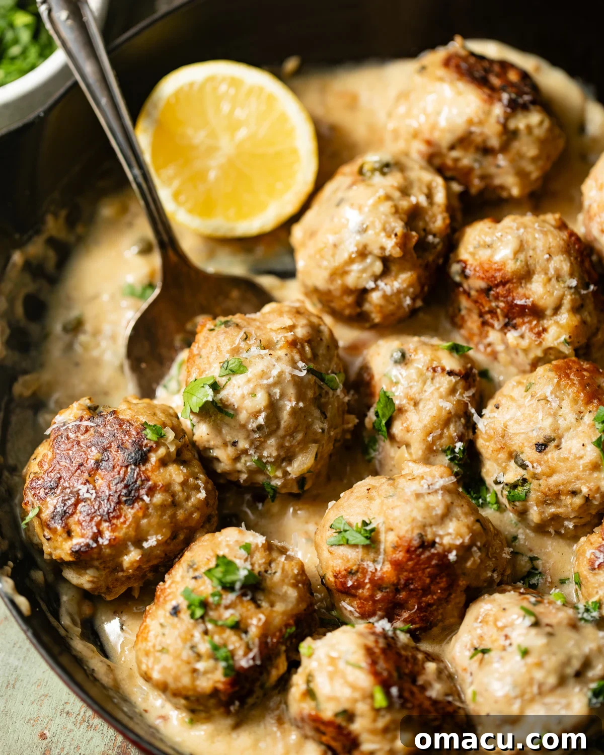 a spoon scooping chicken piccata meatballs out of a skillet.