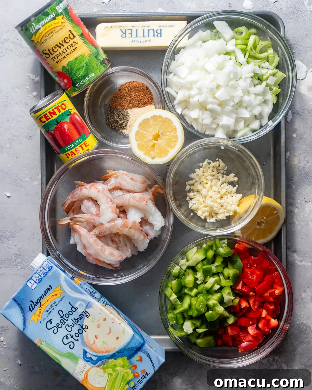 ingredients to make shrimp creole on a tray - large shrimp, seasonings, butter, olive oil, onion, bell pepper, celery, garlic, tomato paste, stewed tomatoes, seafood stock, heavy cream, worcestershire sauce, and hot sauce.