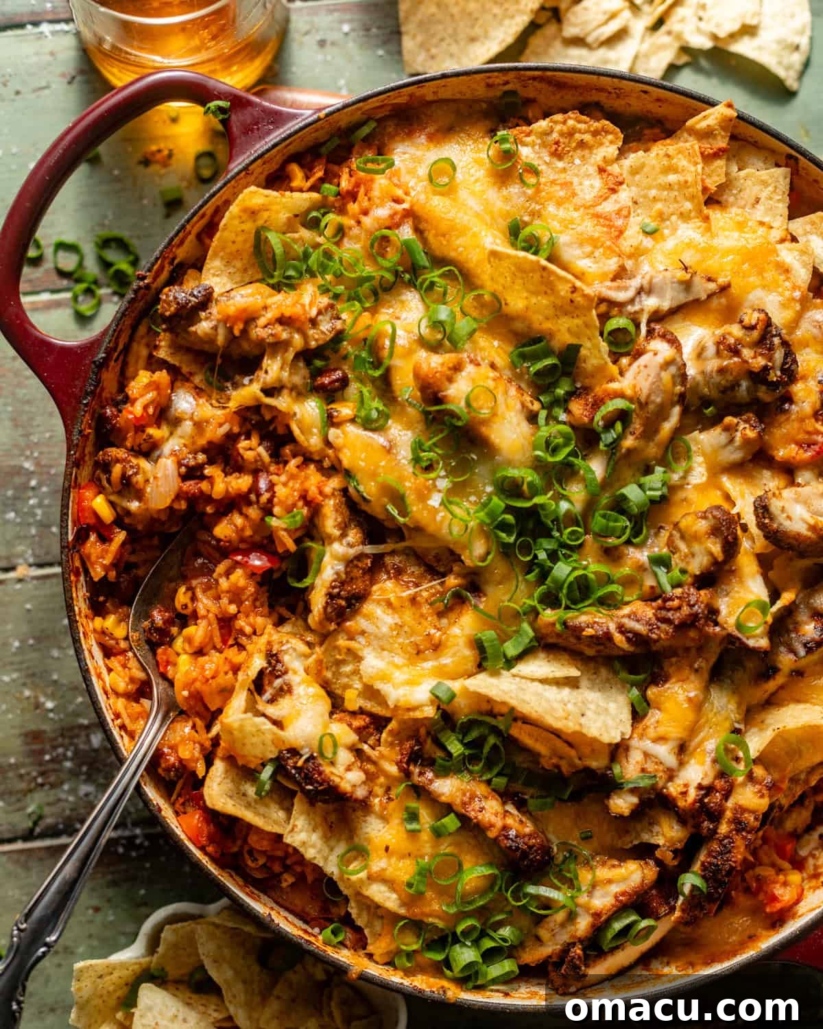 A large skillet brimming with golden, cheesy Mexican chicken and rice, topped generously with crunchy tortilla chips and vibrant green onions.