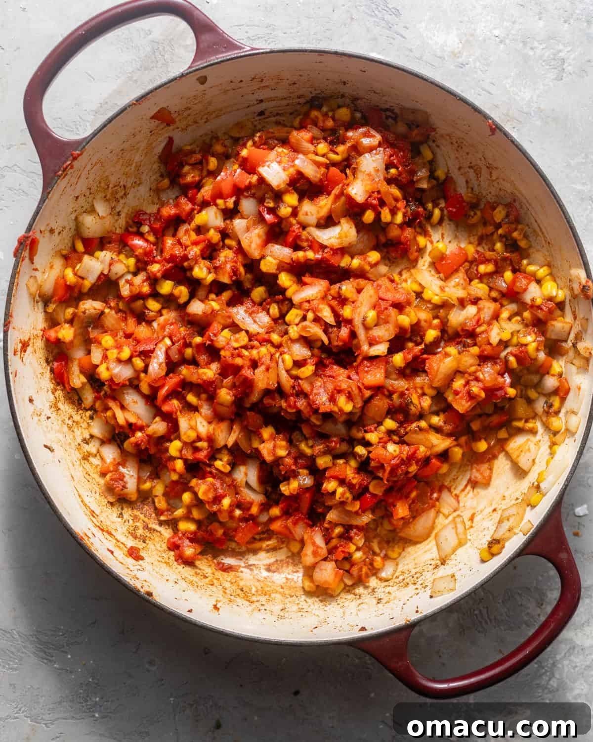 Diced onions, red bell pepper, and garlic being sautéed with corn, rice, salsa, and tomato paste in a large skillet, creating a fragrant base for the Mexican rice.