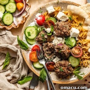 greek meatballs and orzo in a bowl with cucumbers, tomatoes, feta, and pita bread.