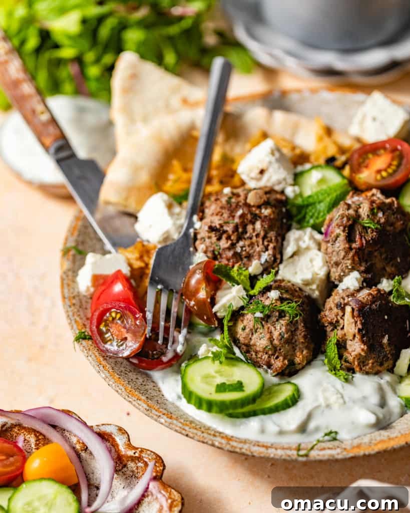 Close-up of Greek meatballs in a bowl, served with tzatziki sauce, fresh tomatoes, and cucumbers for garnish.