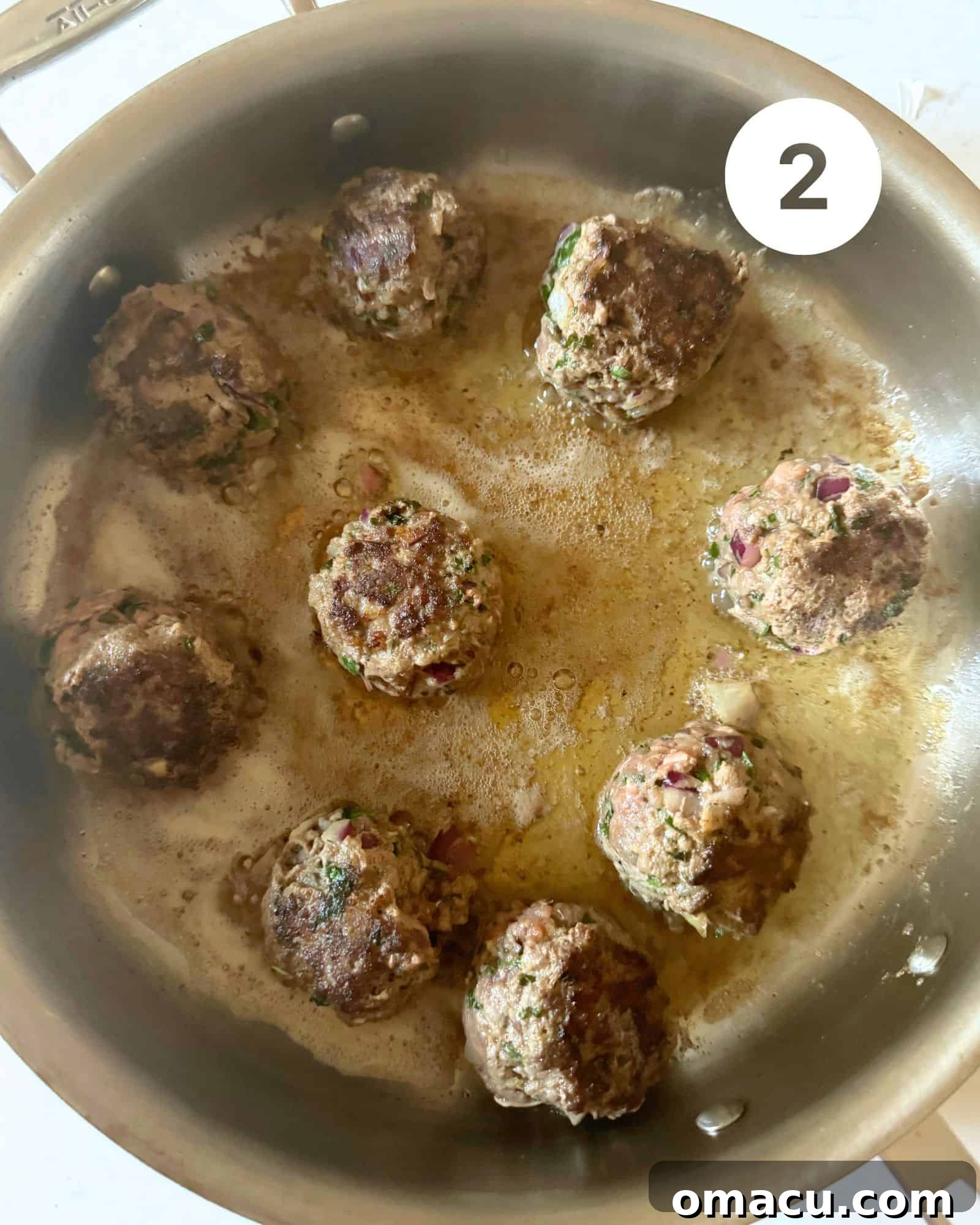 Greek meatballs browning in a large skillet, being cooked in batches.