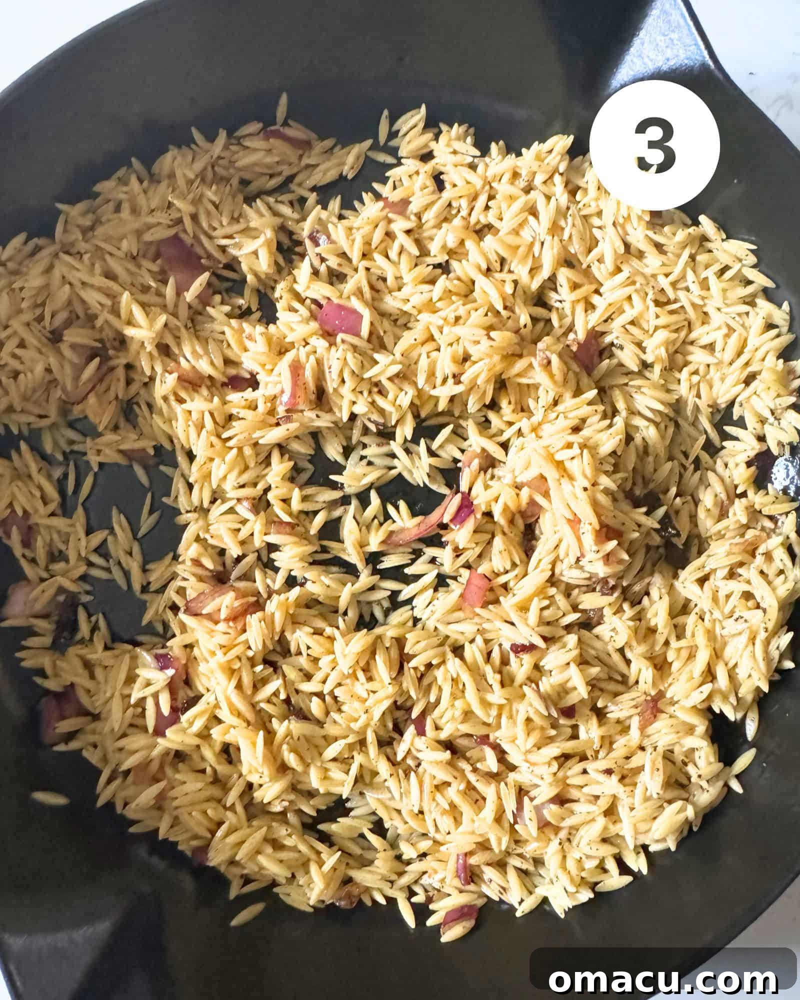 Orzo pasta being toasted in a cast iron skillet with garlic and water, absorbing the flavors.