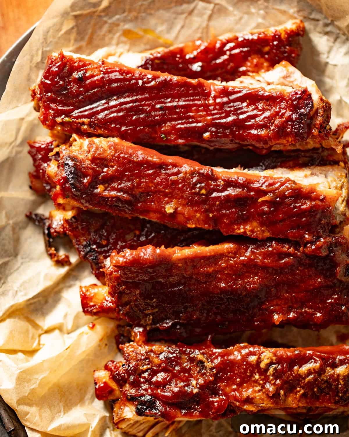 Close-up of perfectly cooked oven-baked ribs on parchment paper, glistening with barbecue sauce.