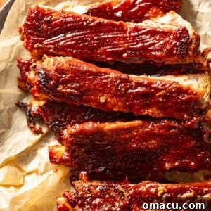 up close photo of oven baked ribs on a piece of parchment paper covered in bbq sauce.