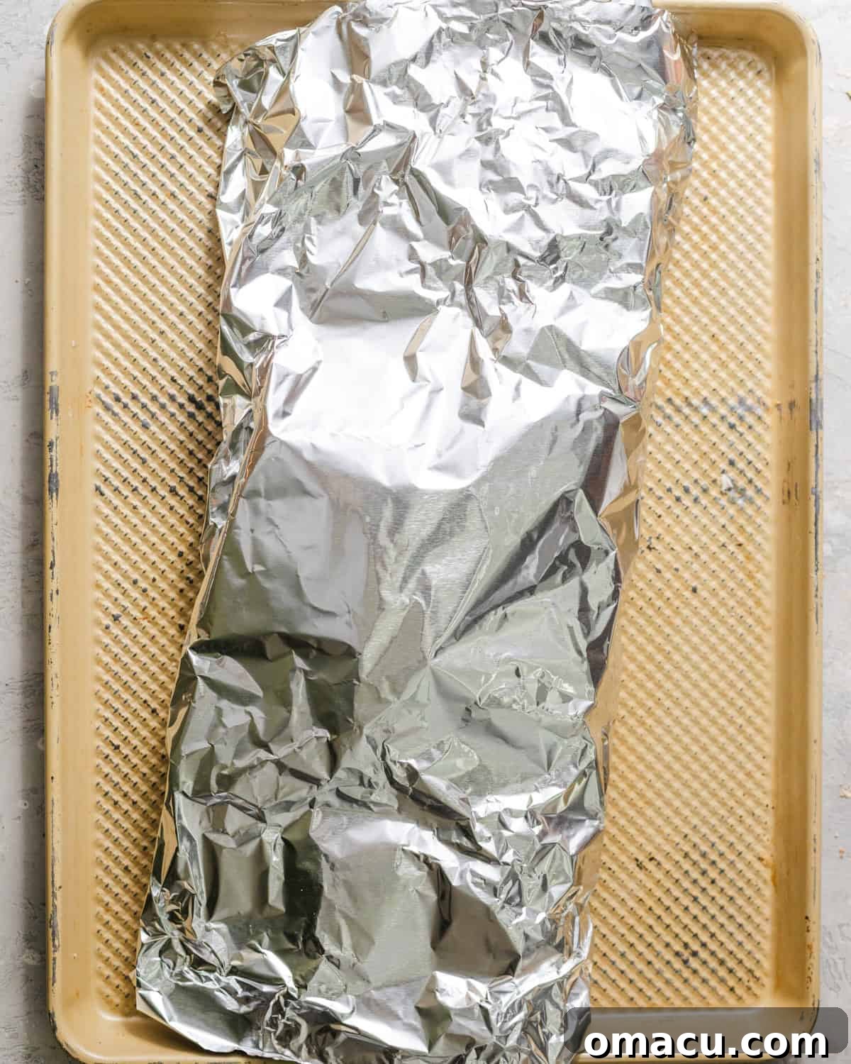 Ribs fully covered and sealed in aluminum foil on a baking sheet.