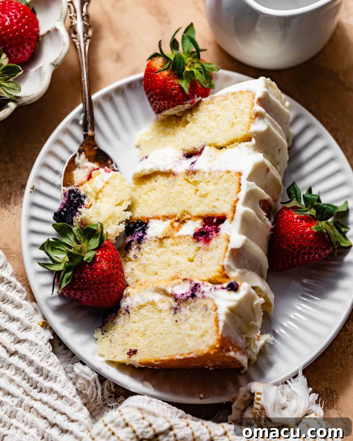 A beautifully sliced Berry Chantilly Cake on a white plate, adorned with fresh mixed berries and a fork, ready to be enjoyed.