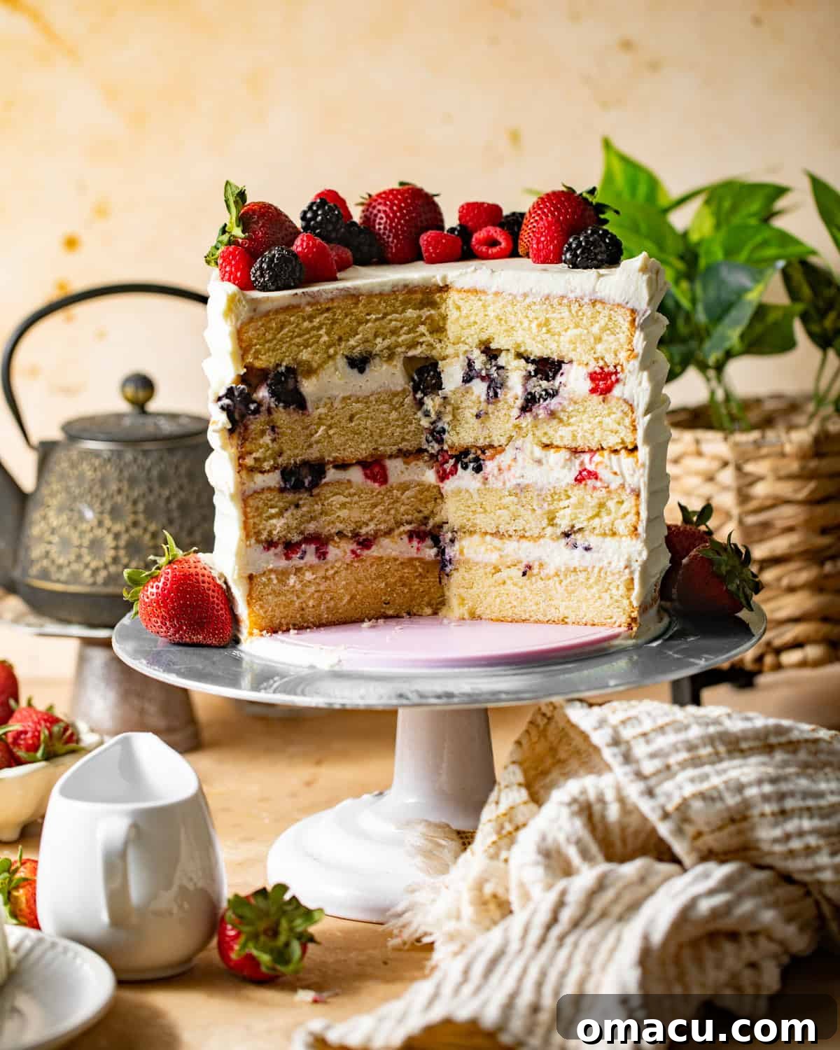 A close-up view of a slice of Berry Chantilly Cake on a cake stand, revealing its beautiful layers of vanilla cake, cream frosting, and fresh berries inside.