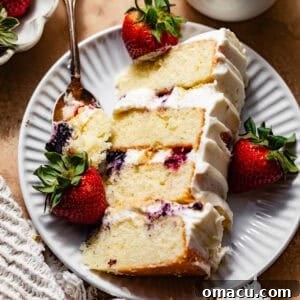 A slice of Berry Chantilly Cake on a plate with fresh berries and a fork, highlighting its beautiful layers and vibrant colors.