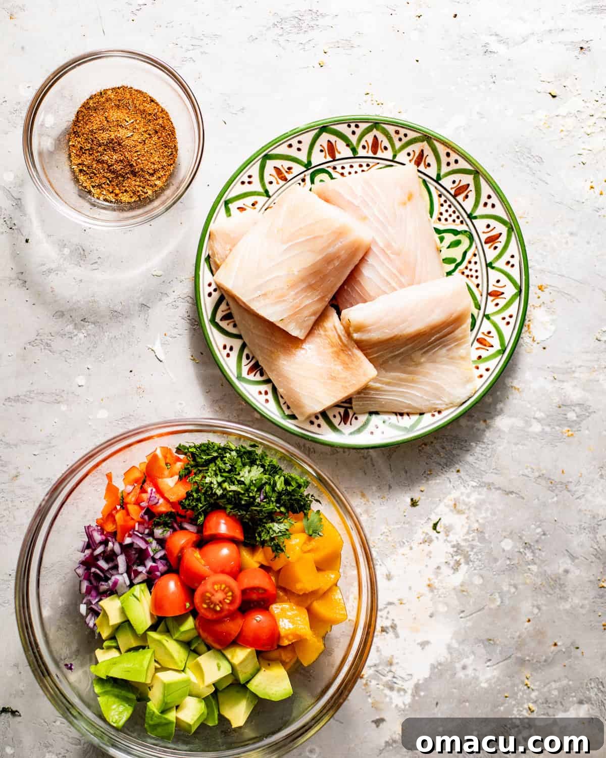 A selection of fresh ingredients laid out on a wooden table, including raw mahi mahi fillets, a bowl of homemade blackening seasoning, and a vibrant bowl of freshly mixed peach salsa, all ready for preparation.
