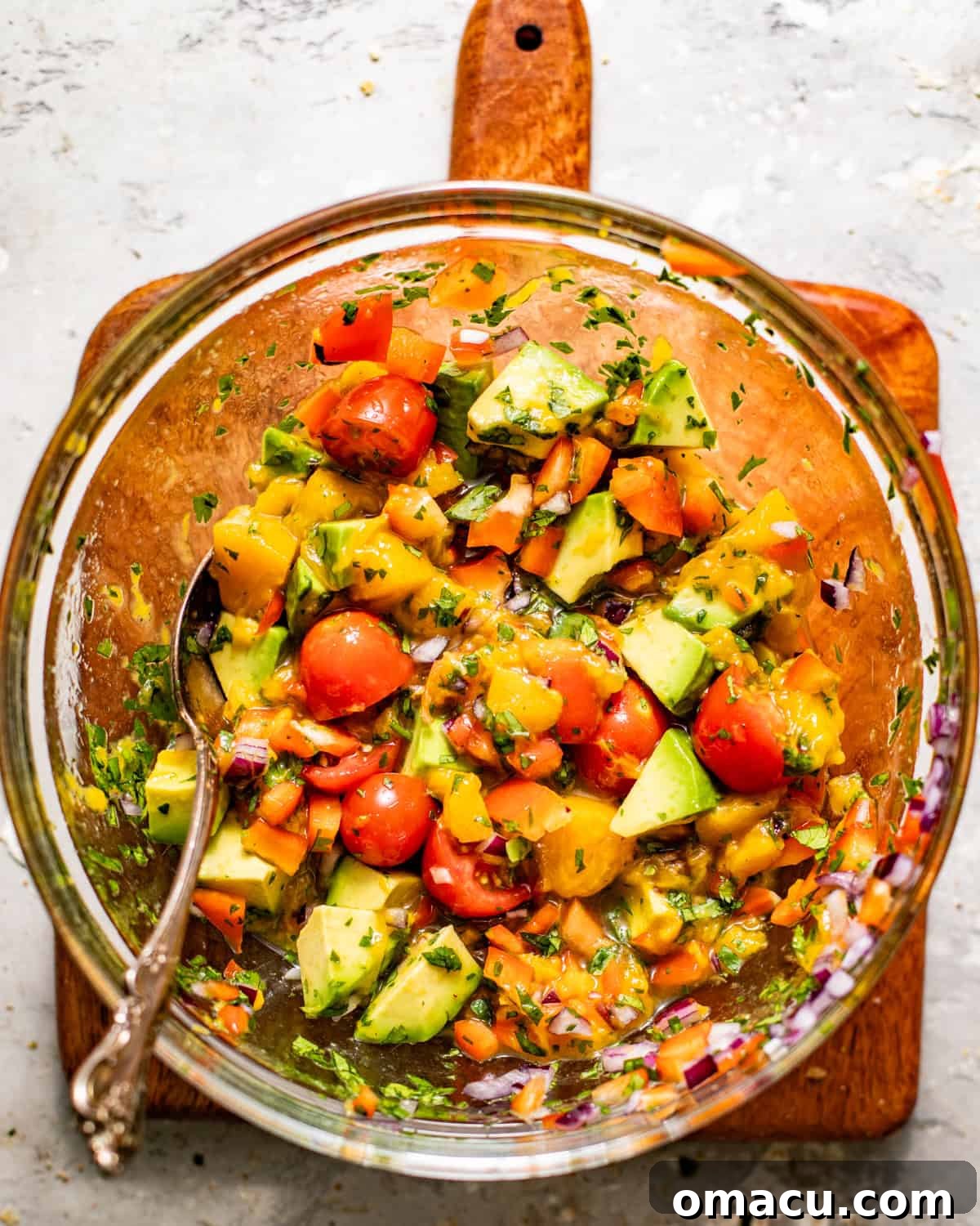 A vibrant, freshly prepared peach salsa, featuring diced peaches, avocado, red onion, bell pepper, tomatoes, cilantro, and lime juice, mixed in a bowl, ready to be served.