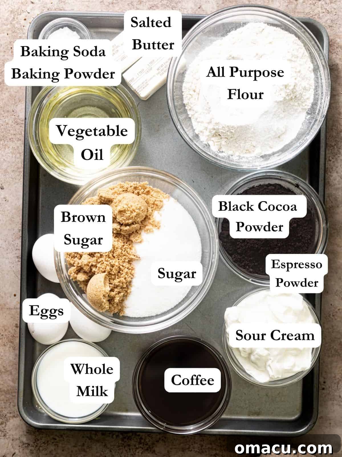 A collection of key ingredients, including cocoa powder, butter, eggs, sugar, and sour cream, arranged on a baking sheet, ready for making chocolate cake.
