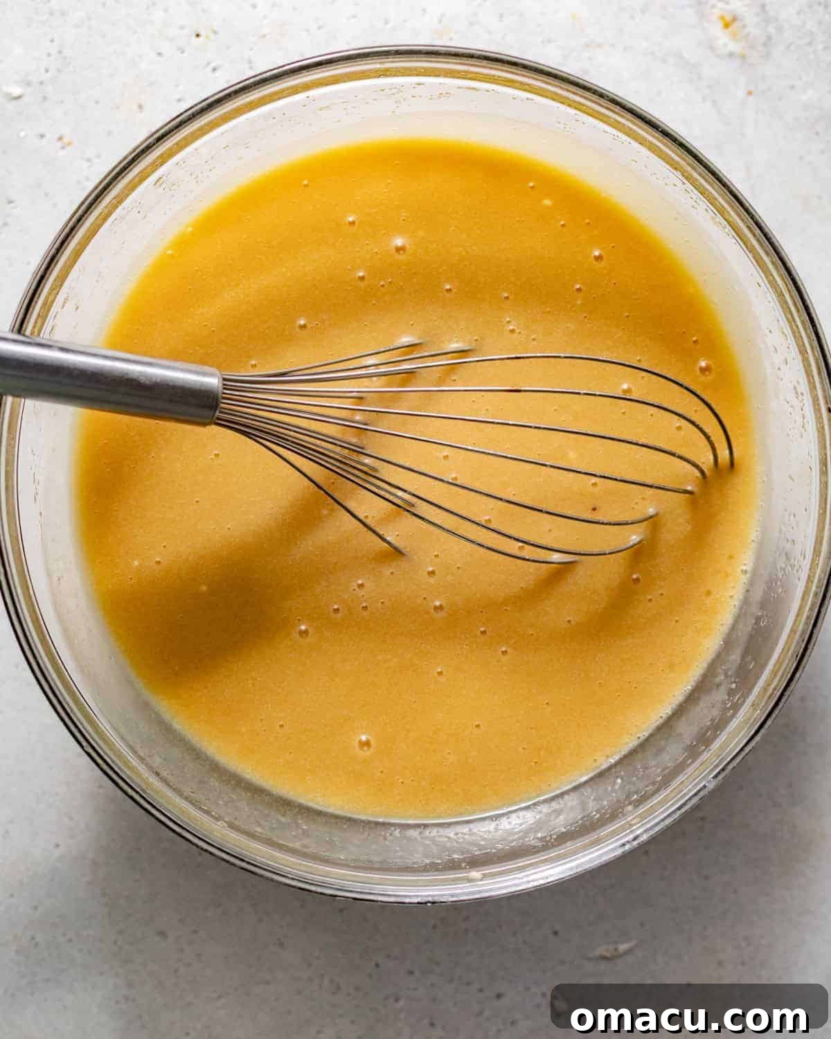 Wet ingredients, including vegetable oil, melted butter, sugar, eggs, and egg yolks, are whisked together in a large mixing bowl until smooth and well combined.