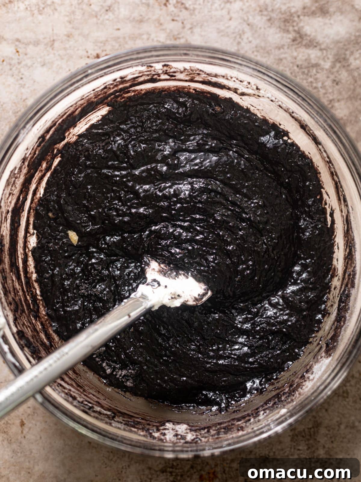 The chocolate cake batter is shown in a large mixing bowl after all ingredients except hot coffee have been combined, exhibiting a thick and rich consistency.
